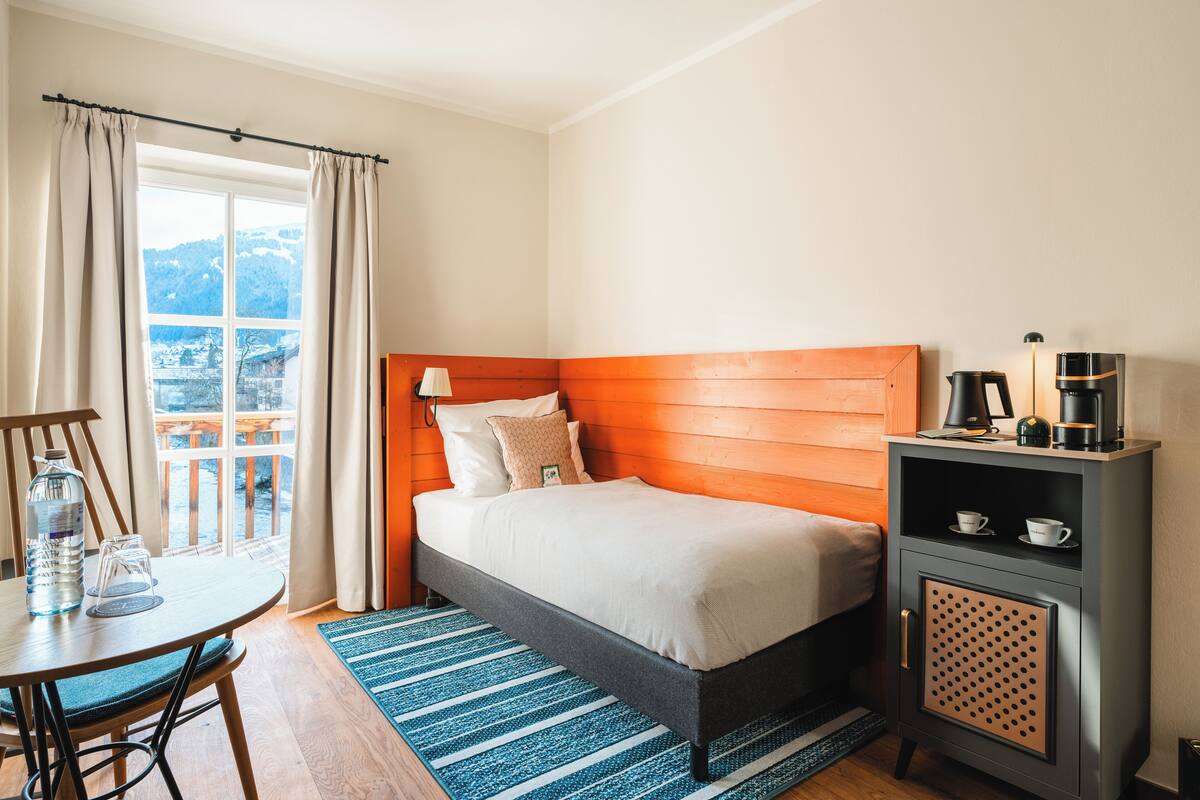 A neatly arranged hotel room with a bed, a small table with a chair, a coffee maker, and a view of the outdoors.