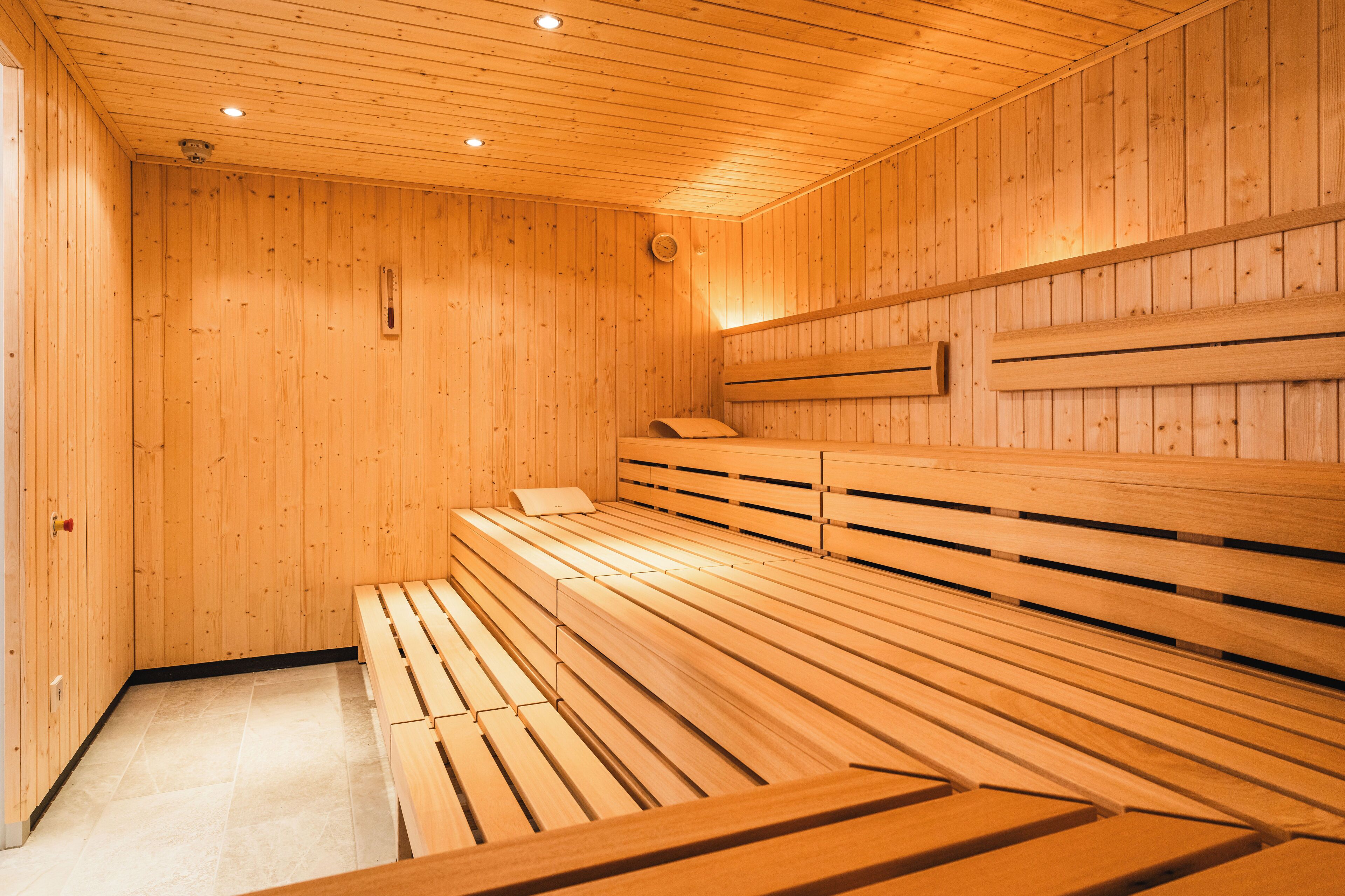 Una sauna con bancos y paredes de madera, un termómetro visible y una puerta.
