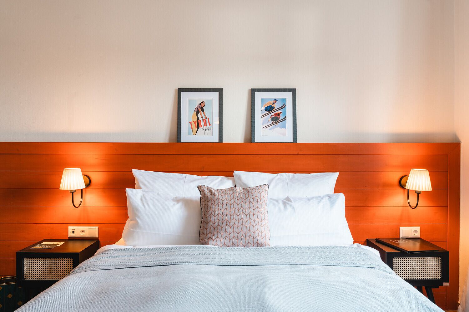 Ein Hotelzimmer mit einem hölzernen Kopfteil, zwei gerahmten Bildern, weißer Bettwäsche und Nachttischlampen.