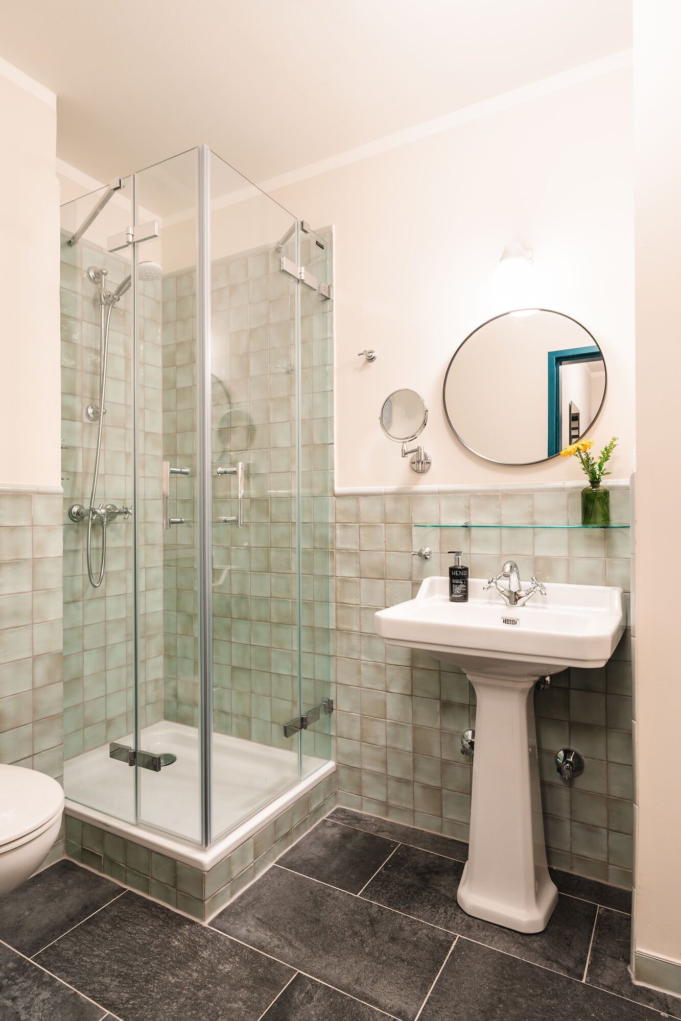 Un baño con ducha de vidrio, lavamanos pedestal y espejo.