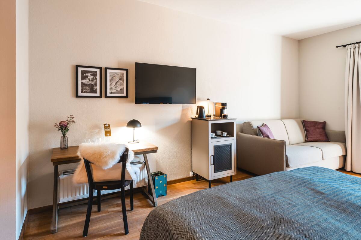 A hotel room with a bed, a desk with a chair, a sofa, a television, and a cabinet.