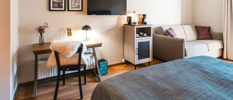 A hotel room with a bed, a desk with a chair, a sofa, a television, and a cabinet.