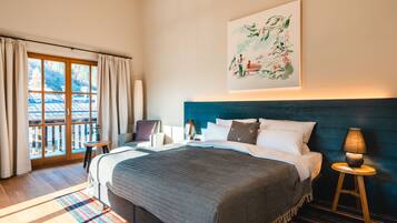 A bedroom with a large bed, a view through a sliding door, a painting on the wall, and a nightstand with a lamp.