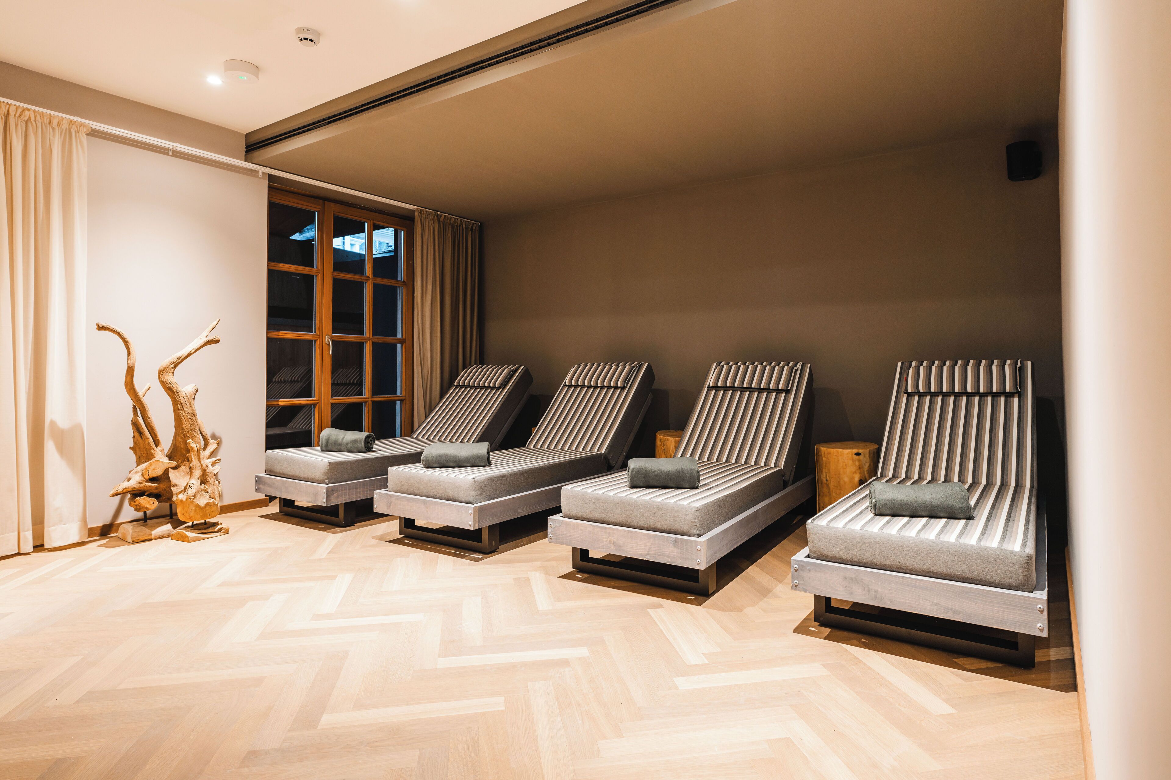 Een kamer met drie ligstoelen, een houten sculptuur en een groot raam.