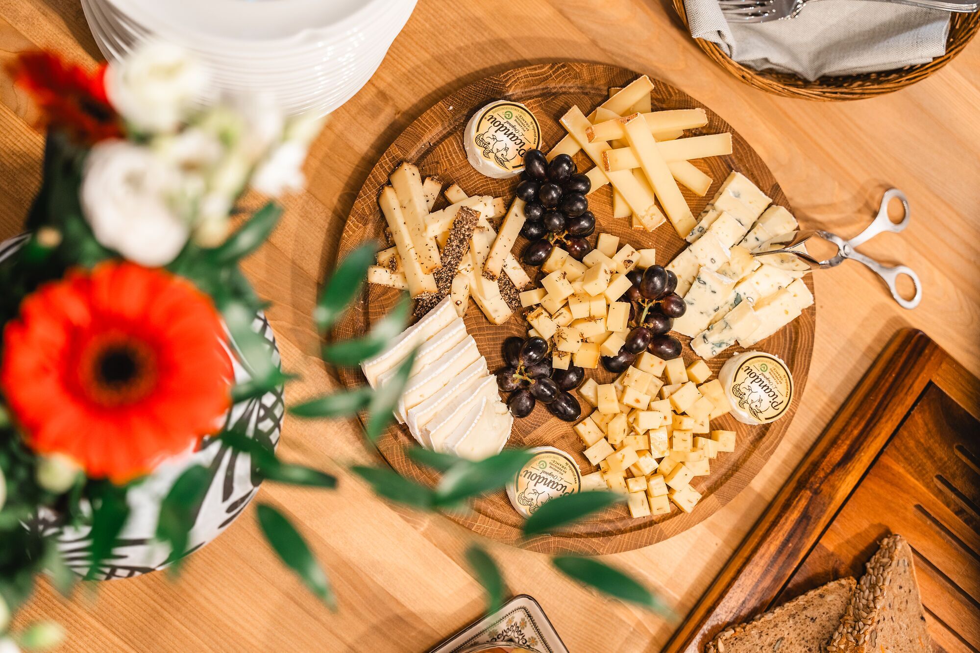 Una tabla de madera con varios quesos, uvas y un recipiente pequeño de mantequilla.