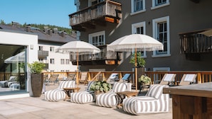 A rooftop lounge area with striped lounge chairs, white umbrellas, and a wooden table.
