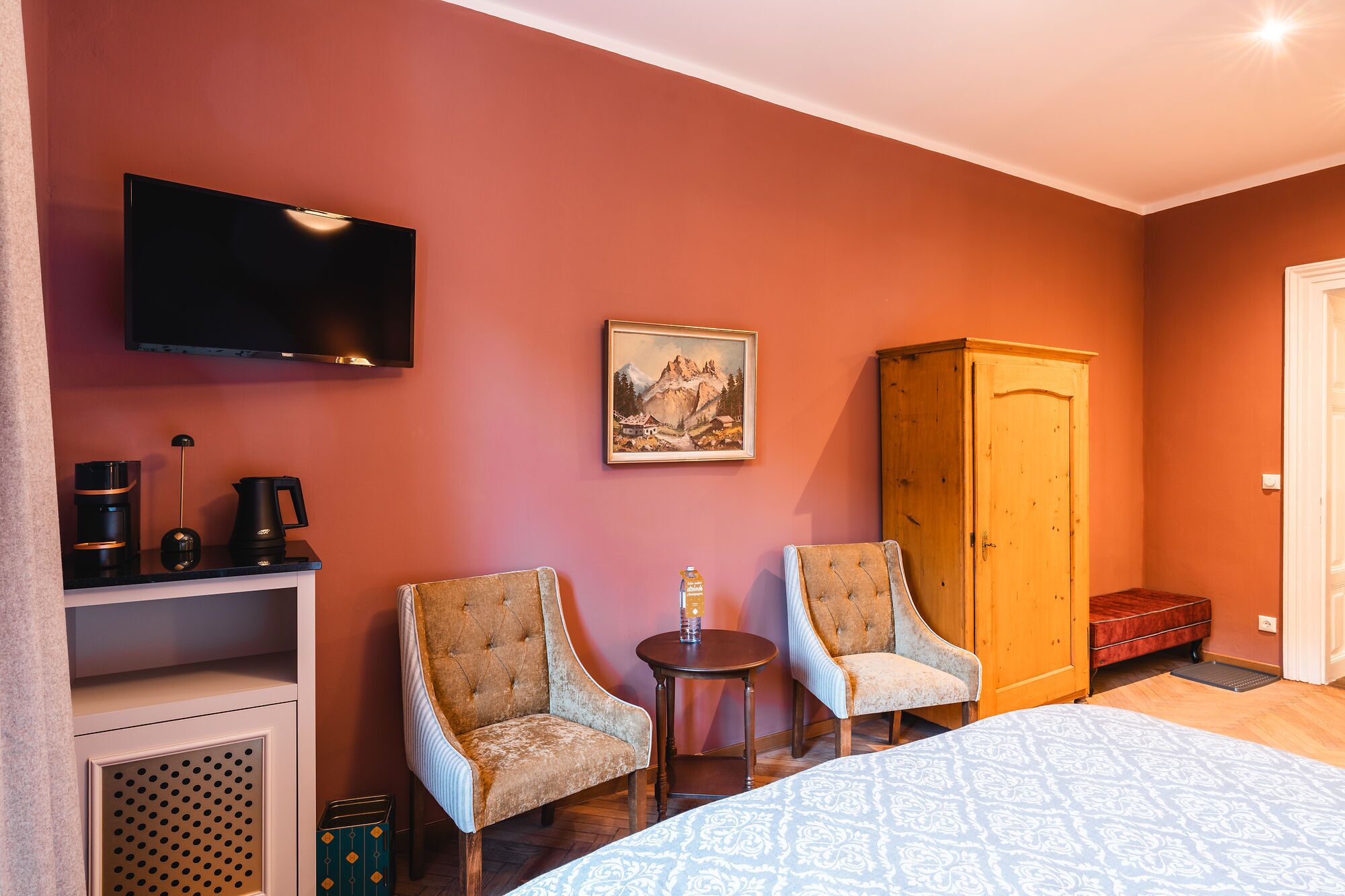 Habitación de hotel con cama, dos sillones, una mesita, televisor, un cuadro y armario.
