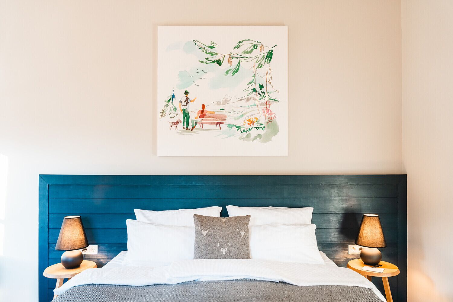 Un dormitorio con cabecera azul, ropa de cama blanca y dos lámparas de noche.