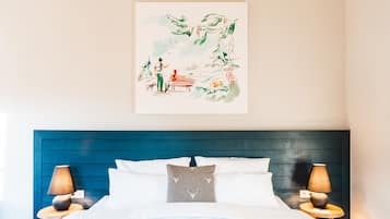 Un dormitorio con cabecera azul, ropa de cama blanca y dos lámparas de noche.