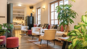 A spacious living area with a sofa, armchairs, and a coffee table. There are several potted plants and a television mounted on the wall.
