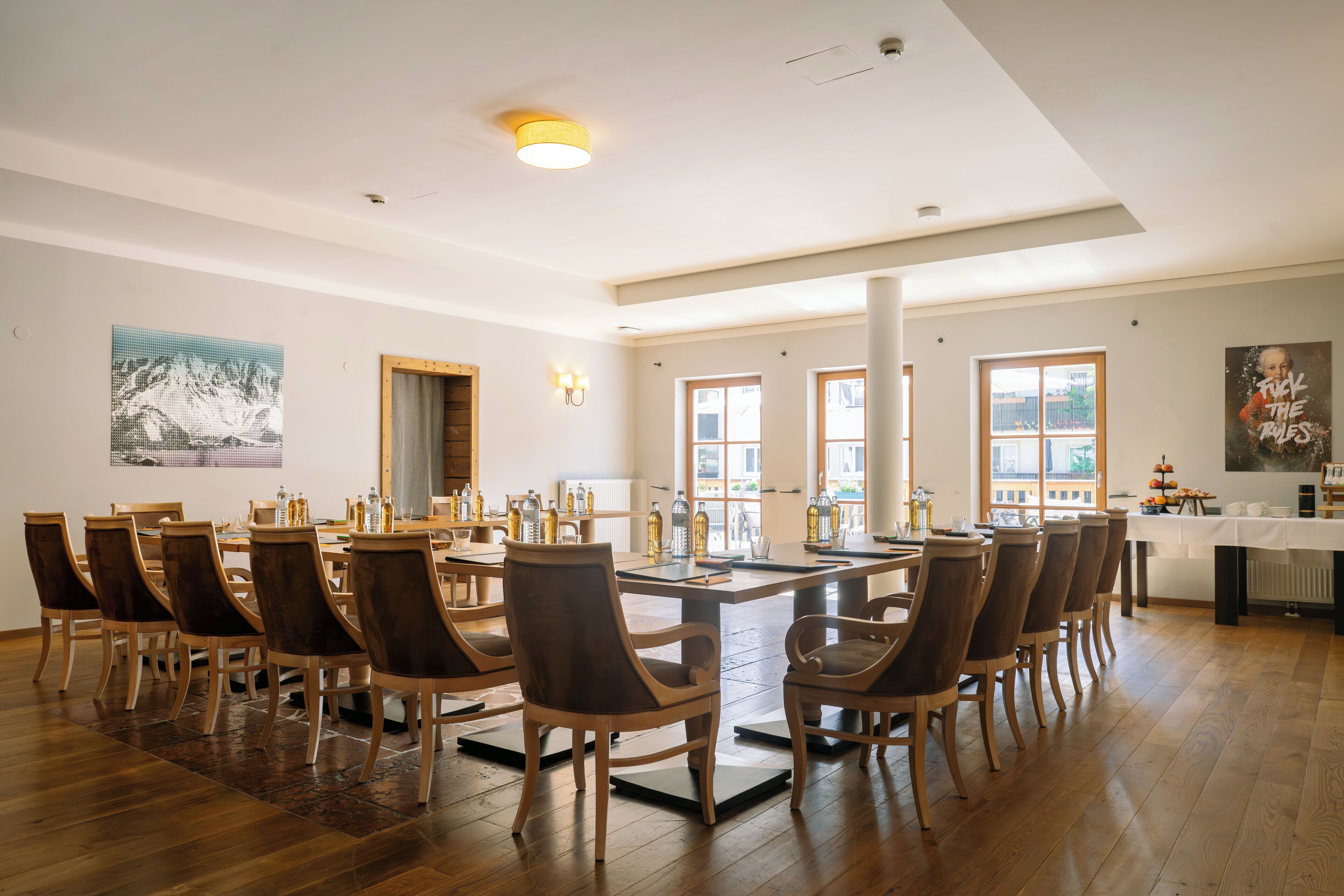 Un comedor amplio con una gran mesa de madera y sillas, rodeado de ventanas y obras de arte.