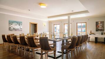 Un comedor amplio con una gran mesa de madera y sillas, rodeado de ventanas y obras de arte.