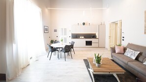 Ett modernt vardagsrum med en matplats, ett kök i bakgrunden och en soffa med kuddar.