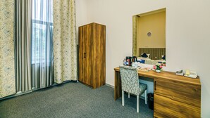 A hotel room with a wooden desk, a chair, a wardrobe, a mirror, and a window with curtains. - Bristol Hotel (Baku)