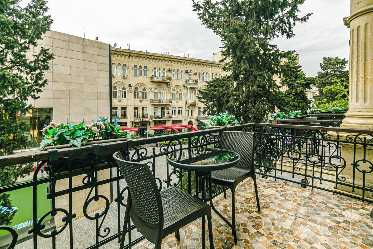 Un balcon avec deux chaises et une table, donnant sur une rue où sont garées des motos et sur un immeuble doté de balcons.