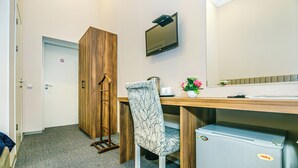 A compact room with a wooden wardrobe, a desk with a chair, a small fridge, a television, and a door with a 'no entry' sign. - Bristol Hotel (Baku)