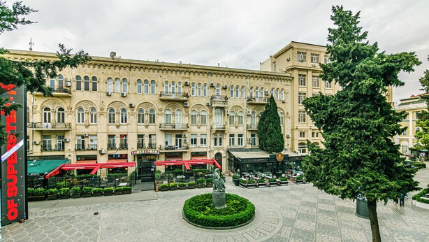 A historic building with a central courtyard, a statue, and surrounding greenery. - Bristol Hotel (Baku)