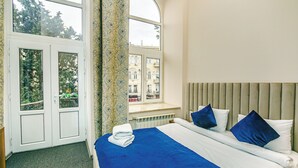 A bedroom with a large bed, a window with a view of buildings, and a radiator under the window. - Bristol Hotel (Baku)