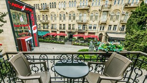 A balcony with two chairs and a table, overlooking a courtyard with a Shakespeare Theatre and a building with ornate architecture. - Bristol Hotel (Baku)