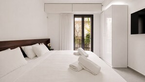 Une chambre d’hôtel moderne dotée d’un grand lit, d’un téléviseur fixé au mur et d’un balcon offrant une vue sur les arbres.