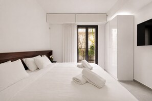 A modern hotel room with a large bed, a TV mounted on the wall, and a balcony with a view of trees.