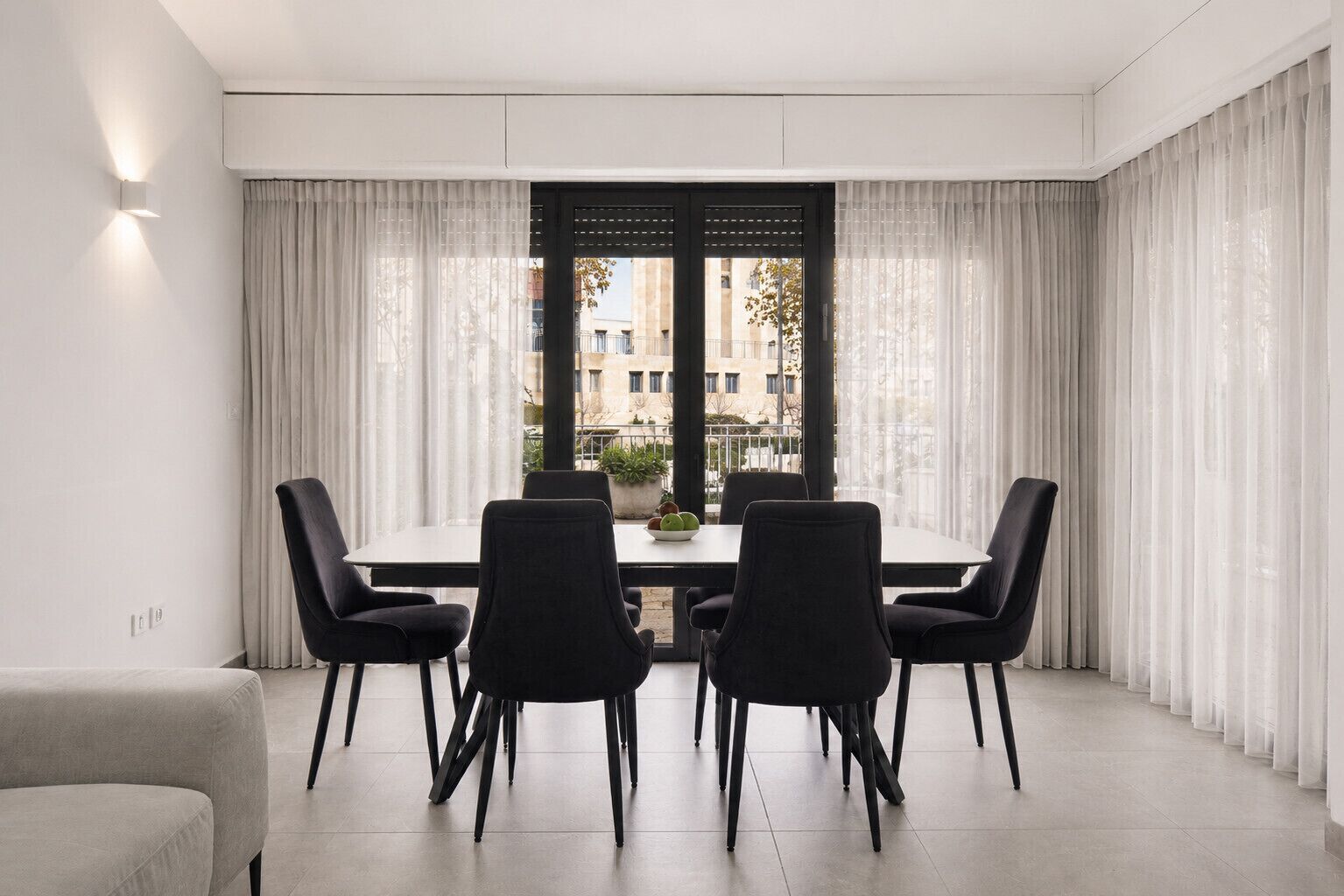 A modern dining area with a table and chairs, a potted plant, and a view through a window with curtains.