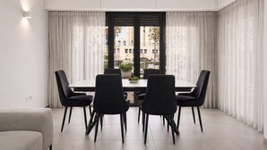 Un espace repas moderne avec une table et des chaises, une plante en pot et une vue sur l’extérieur à travers une fenêtre avec des rideaux.