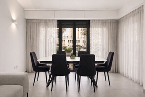 A modern dining area with a table and chairs, a potted plant, and a view through a window with curtains.