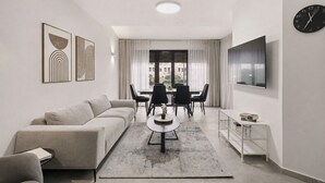 Un salon moderne comprenant un canapé, une table basse, une table à manger avec des chaises, un téléviseur et des œuvres d’art accrochées aux murs.