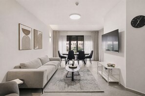 A modern living room with a sofa, coffee table, dining table with chairs, a TV, and artwork on the walls.