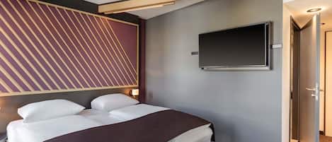 Una habitación de hotel moderna con una cama bien hecha, un televisor de pantalla plana montado en la pared y una puerta que da a otra habitación.