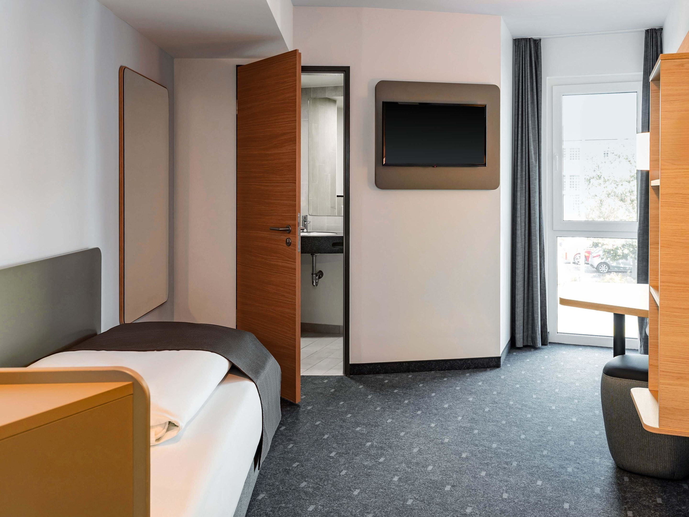 Habitación de hotel con cama, escritorio, televisión y baño visible a través de una puerta abierta.