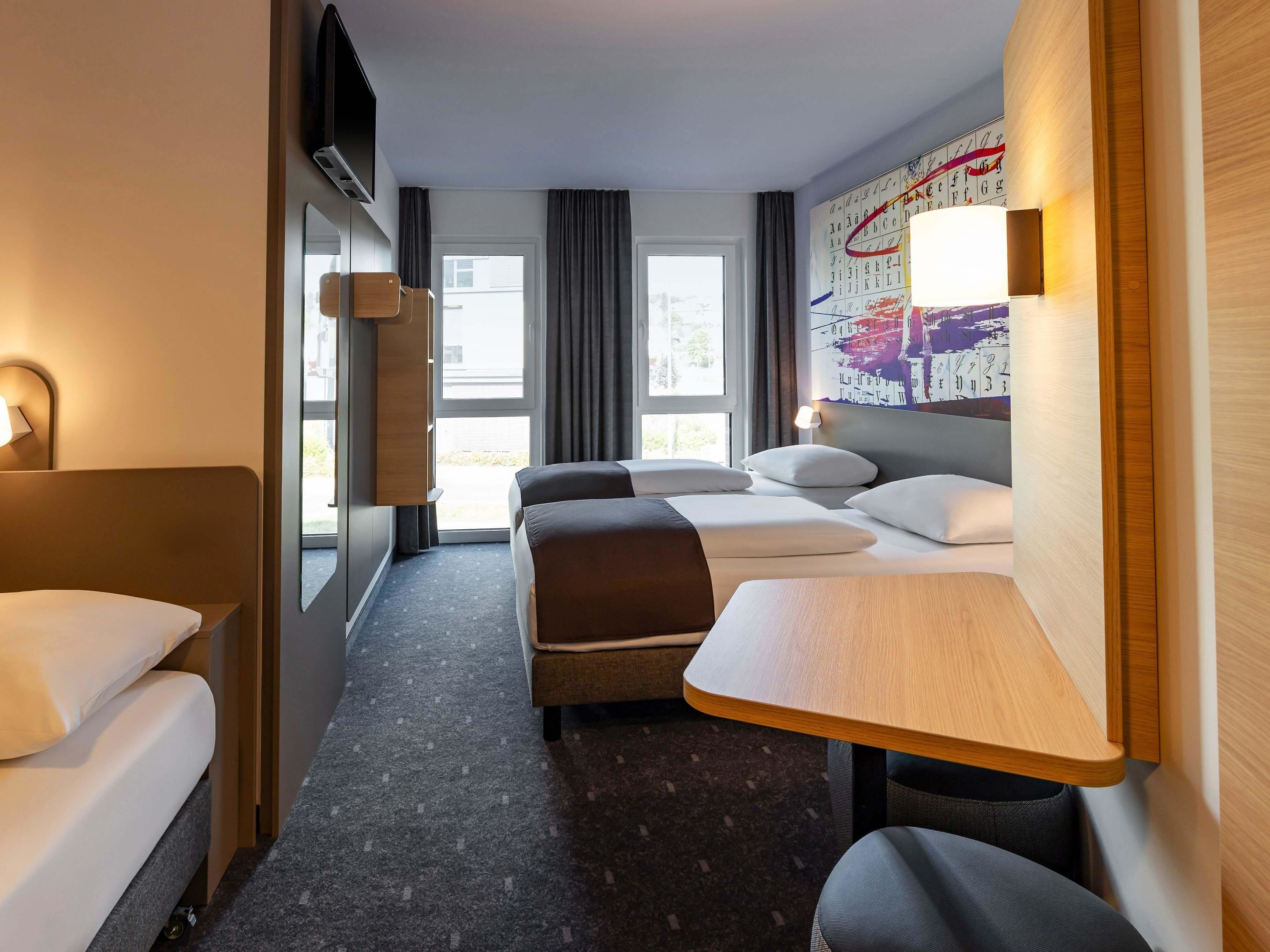 A hotel room with a bed, a desk, a chair, a TV, and a window.