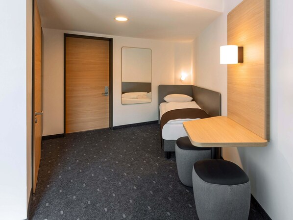 A compact hotel room with a bed, a bedside table, a mirror, and a small stool. - B&B HOTEL Bad Hersfeld (Bad Hersfeld)
