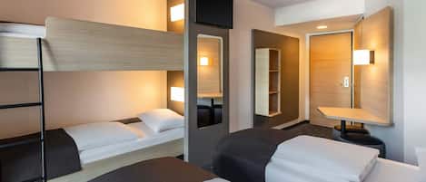 A hotel room with bunk beds, a bedside table with a lamp, a mirror, and a wall-mounted shelf.