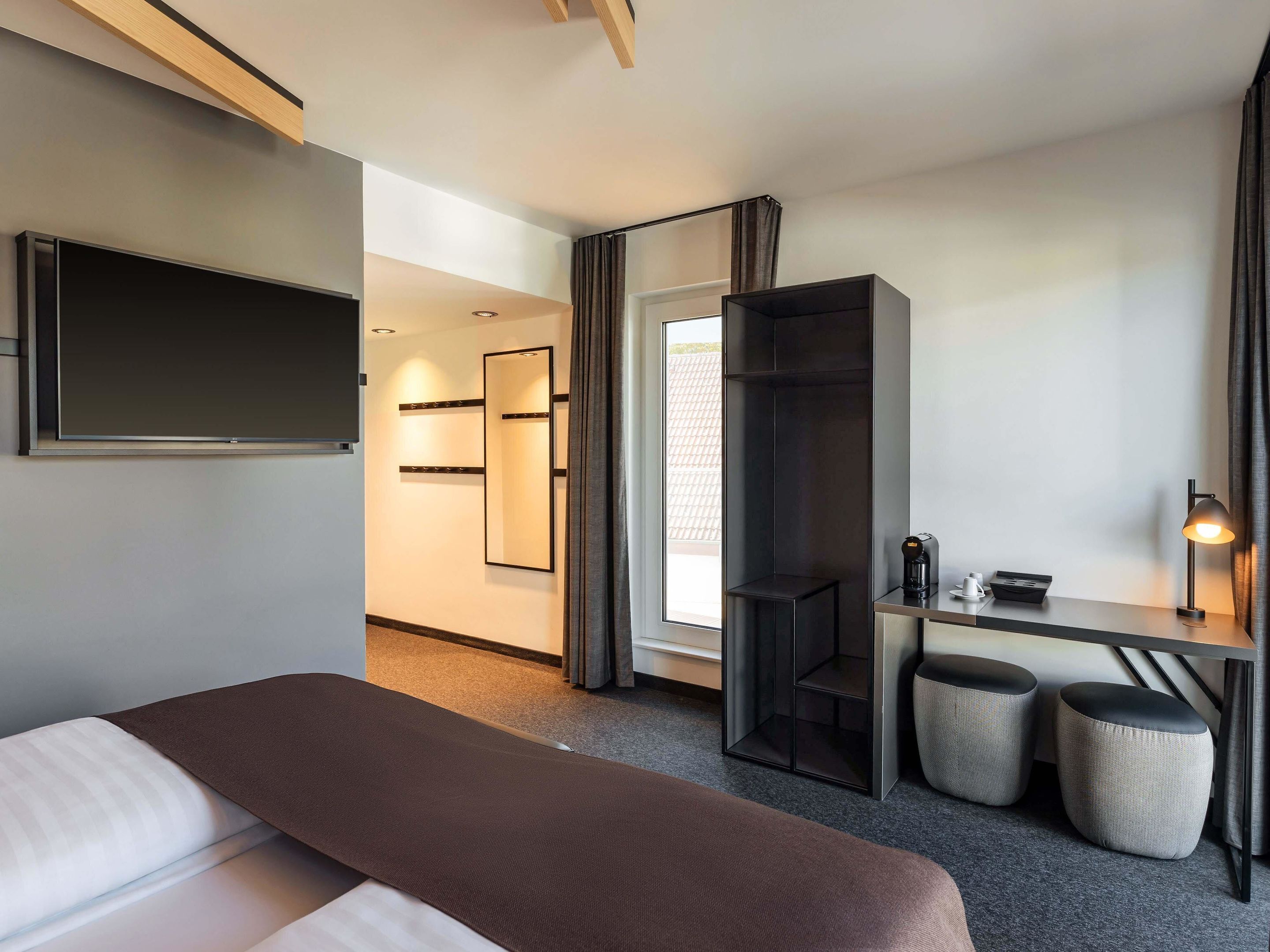 Ein Hotelzimmer mit einem Bett, einem Schreibtisch mit Lampe, einem Spiegel und einem Kleiderschrank.