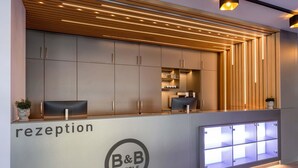 Un área de recepción de diseño moderno, con mostrador de recepción, armarios y el logotipo de B&B Hotels.
