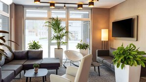 Una sala de estar moderna con un sofá gris, un sillón blanco, una mesita redonda y varias plantas en macetas.