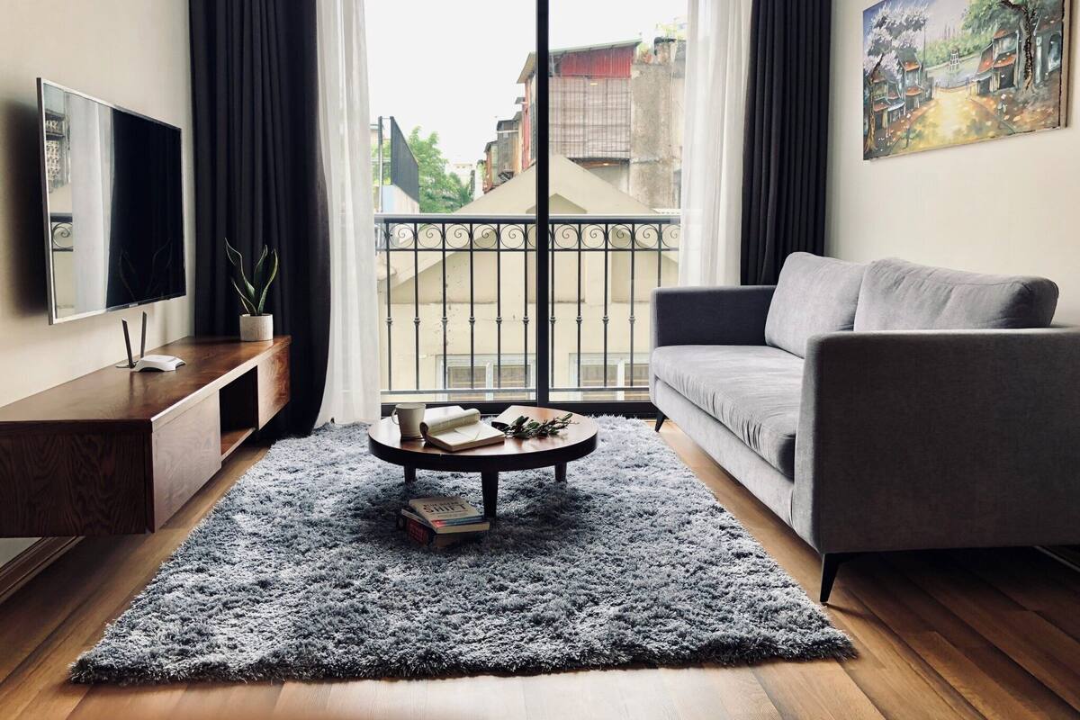 Una sala de estar moderna con un sofá gris, una mesa de centro con libros, un televisor y vistas a un balcón.