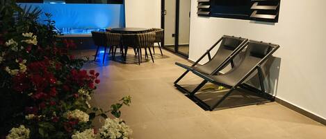 Een buitenterras met een tafel, stoelen, een lounge stoel en een zwembad.