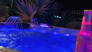 A hot tub with multiple jets and a bottle of alcohol nearby.