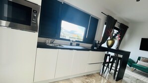 A modern kitchen with a built-in microwave, a large window with curtains, and a view of a building outside.