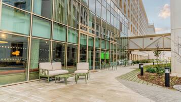 A modern building with large glass windows and a paved outdoor area with seating.