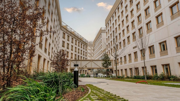 Un edificio moderno con varios pisos, grandes ventanales y un patio central con zonas de estar.