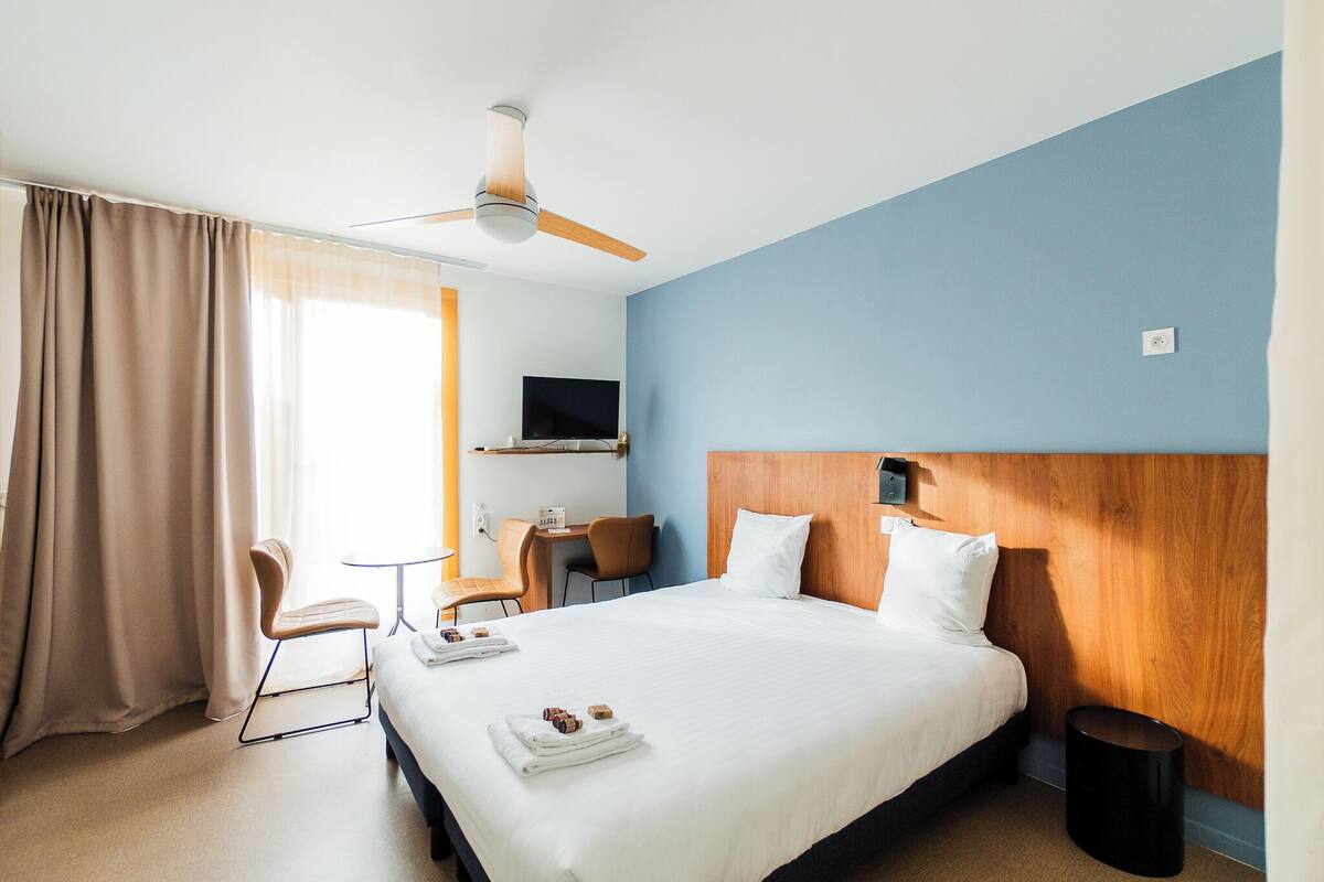 A hotel room with a bed, a desk, a chair, a TV, and a ceiling fan.