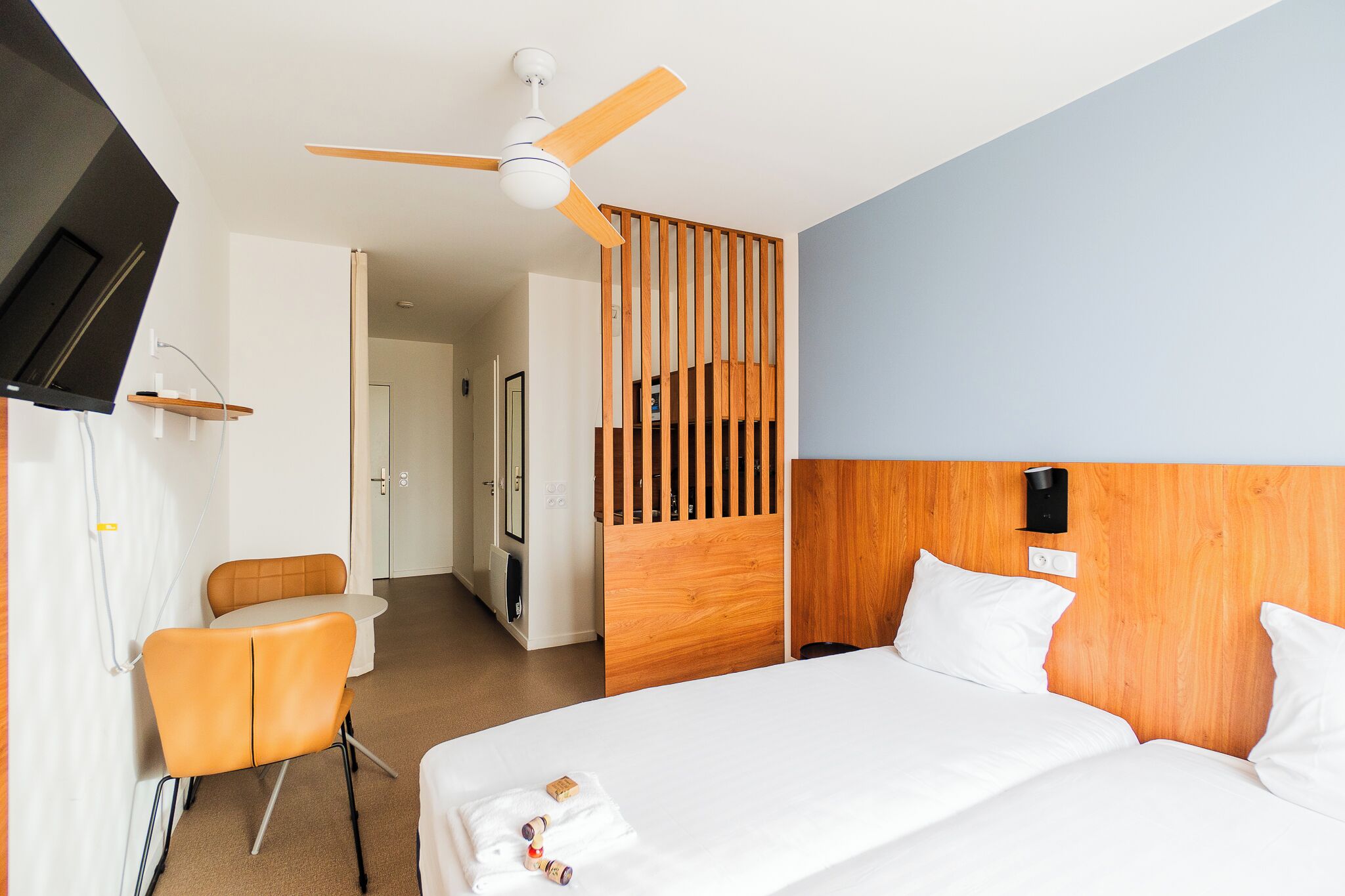 A hotel room with a bed, a chair, a desk, a TV, and a ceiling fan.