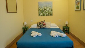 Habitación de hotel con una cama grande, dos mesitas de noche, un cuadro en la pared y una fotografía enmarcada sobre la cama.