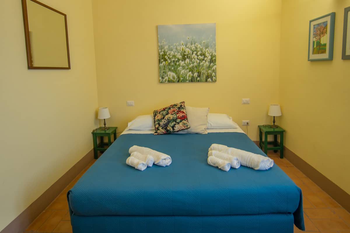 A hotel room with a large bed, two nightstands, a painting on the wall, and a framed picture above the bed.
