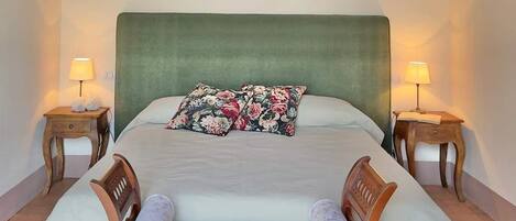 A neatly made bed with a green headboard, two bedside lamps, and a floral pillow.