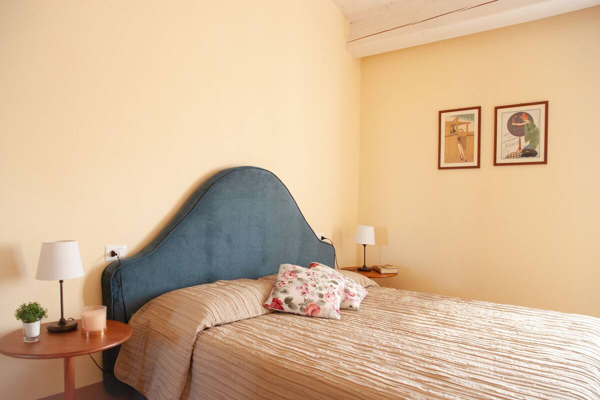 A neatly made bed with a blue headboard, two bedside tables with lamps, and two framed pictures on the wall.